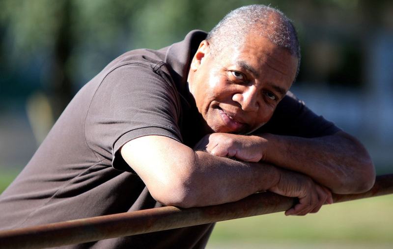 A relaxed man leaning on a railing outdoors, smiling in the sunshine