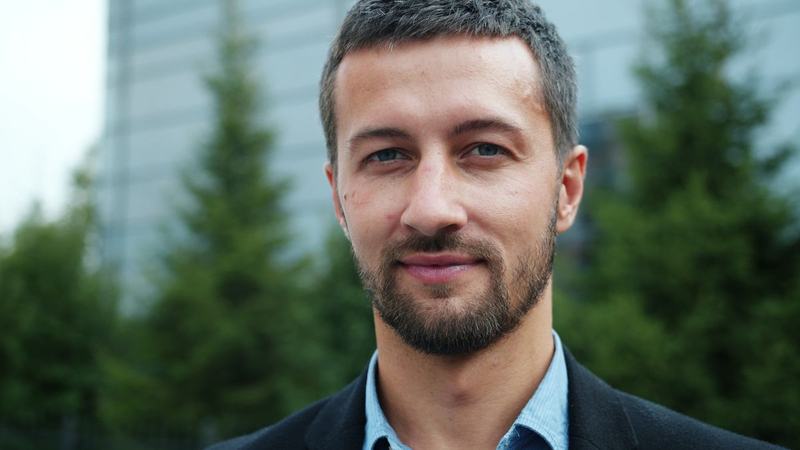 A relaxed, confident man with a greying beard smiling outdoors